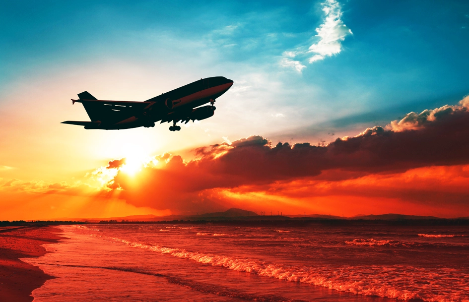 airplane taking off over shoreline beach during sunset