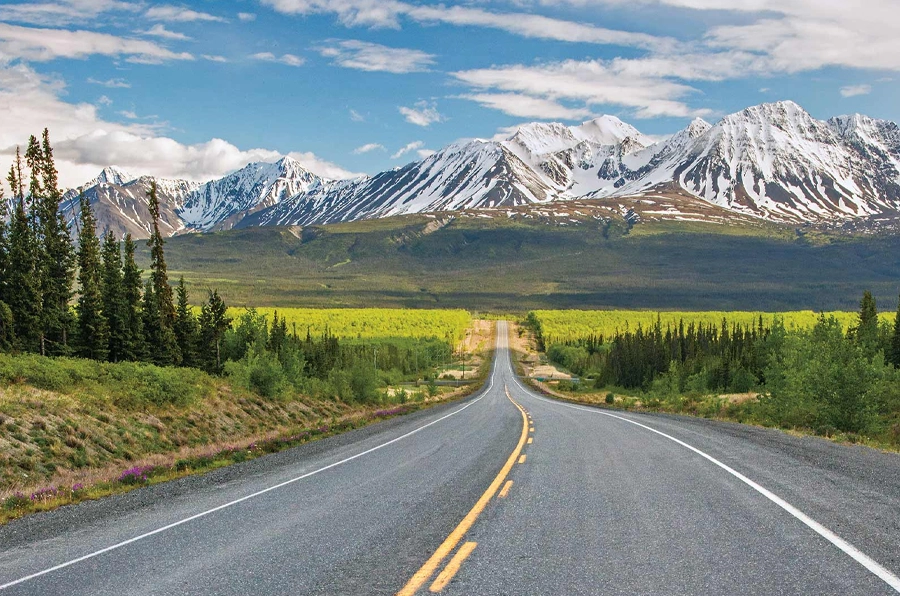 alaska daytime on long straight road with snowy mountains in background