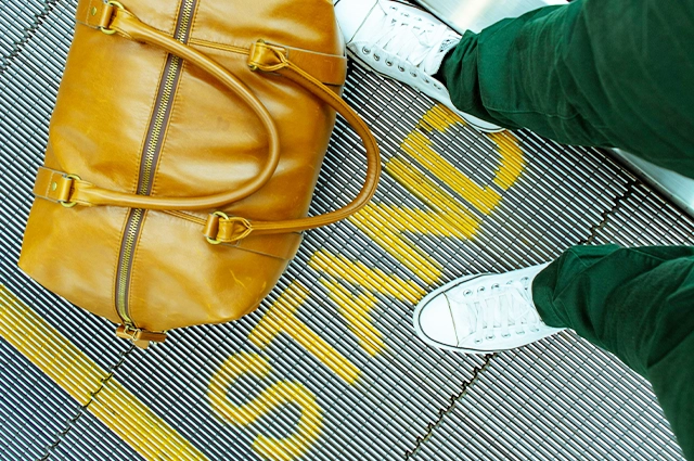 man standing on escalator with leather luggage bag