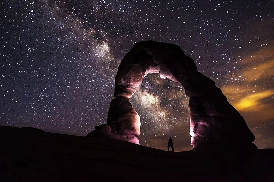 national parks stone formation at night with stars guy standing under rock