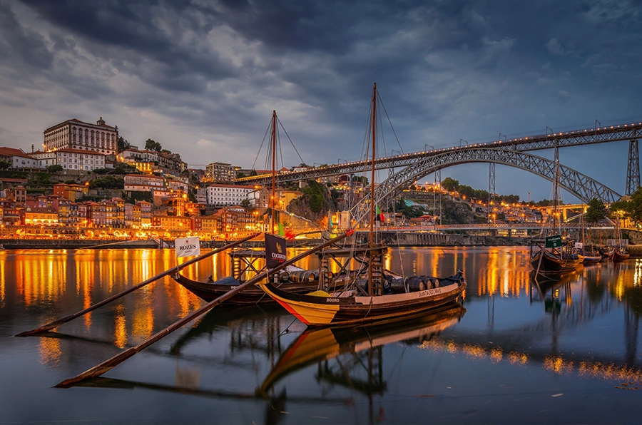 portugal at night with two boats on water overlooking bridge